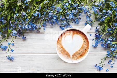 Blaue Vergiss-mich-nicht Blumen und eine Tasse heißen Kaffee auf einem weißen Holztisch Stockfoto