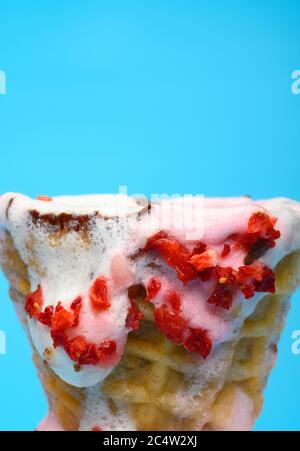 Eis-Konus mit Vanille- und Erdbeergeschmack in einem Schmelzprozess aus der Nähe auf blauem Hintergrund Stockfoto