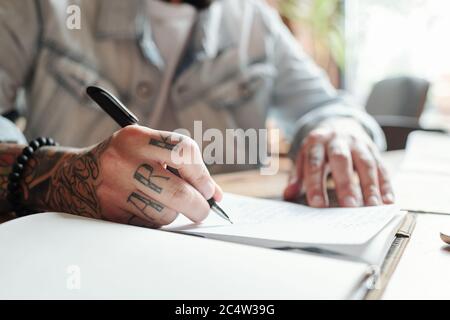 Nahaufnahme eines nicht erkennbaren Mannes, der am Tisch sitzt und Pläne auf dem Notizblock aufschreibt Stockfoto