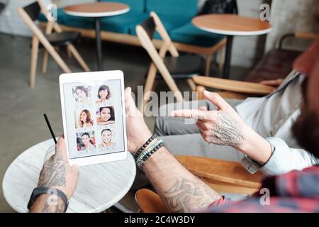 Über die Schulter Ansicht von tätowierten Mann Mädchen Fotos mit Dating-App anzeigen, während es mit Freund im Café diskutieren Stockfoto