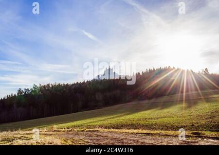 Grünes Feld und Wald unter der hellen Sonne und blauen Himmel mit einem alten Schloss auf dem Hintergrund Stockfoto