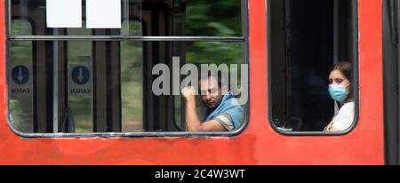 Belgrad, Serbien - 25. Juni 2020: Menschen mit chirurgischen Gesichtsmasken, während sie auf einem Fenstersitz einer fahrenden Straßenbahn sitzen und reiten, von außen Stockfoto