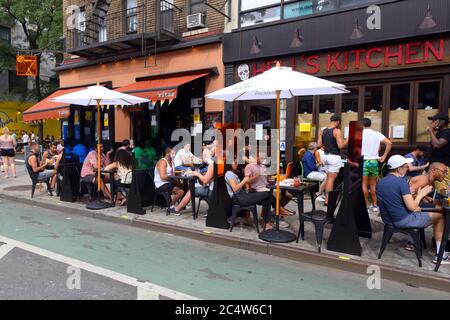 New York, NY, 28. Juni 2020. Leute, die Getränke halten und sich außerhalb von 'Ritas auf der Ninth Avenue in der Hells Kitchen Nachbarschaft unterhalten. Tische mit bunten Trennwänden wurden auf dem Bürgersteig für gesellschaftlich distanzierte Mahlzeiten im Freien im Rahmen der Phase 2 Wiedereröffnung von New York City eingerichtet. Stockfoto