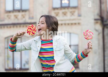 Kind im Süßwarenladen. Frühling Mode-Stil. Fröhliche kleine Mädchen hat süßen Look. Lässig und positive Hipster. Kindheit Glück. Stilvolle Schulmädchen halten Lollipop Süßigkeiten. Verloren in ihrem Märchen. Stockfoto