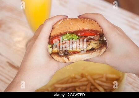 Selektive Aufnahme einer Person, die einen leckeren Hamburger hält Mit Pommes auf dem Tisch Stockfoto