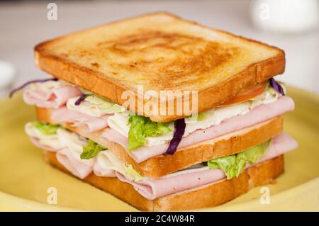 Selektive Fokusaufnahme eines Schinkensandwiches in einem gelben Platte Stockfoto