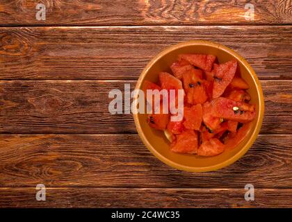 High-Angle-Schuss von in Scheiben geschnittenen Wassermelonen in einer orangefarbenen Schüssel Auf einer hölzernen Oberfläche Stockfoto