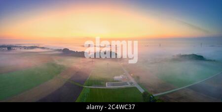 Nebliger Blick über ein Feld bei Sonnenaufgang und Strommast Stockfoto