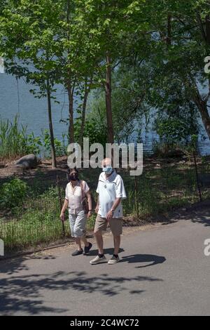 Ein Paar mittleren Alters, das chirurgische Masken trägt, macht einen Übungsspaziergang um den See im Kissena Park, Flushing, Queens, New York City. Trägt, trägt, Stockfoto