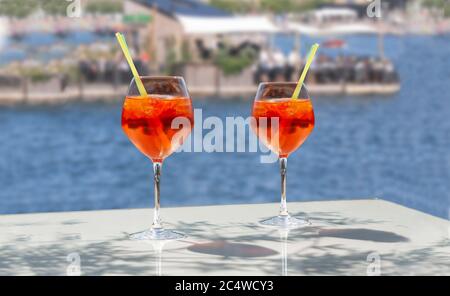 Nahaufnahme von zwei Gläsern gekühlter Cocktailgetränke mit Strohhalmen und Eiswürfeln auf einem Tisch in Strandnähe. Blaues Wasser und Leute in einem Strandrestaurant i Stockfoto