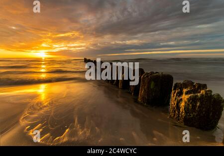 Schöner Sonnenuntergang an der Ostsee, Wellen waschen die alten hölzernen Wellenbrecher Stockfoto