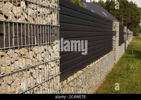 Ein Fragment eines langen Zauns eines Hauses, das mit Hilfe von Gabionen gemacht wurde. Stockfoto