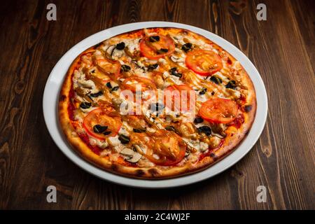 Pizza mit Hühnerfleisch, Pilzen, Tomaten und schwarzen Oliven, Holzhintergrund, Low-Key Stockfoto