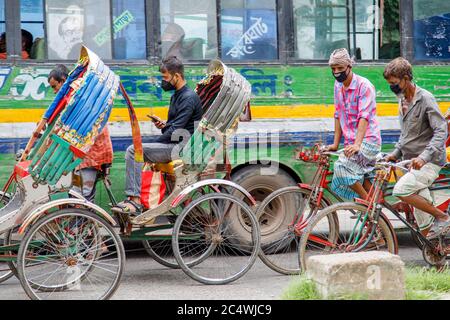 Ricksha-walas, oder Rikscha-Fahrer mit ihren Passagieren auf den Straßen von Dhaka. Die Bewohner der Hauptstadt Dhaka in Bangladesch stellen sich der Bedrohung durch den Corona-Virus COVID 19. Stockfoto