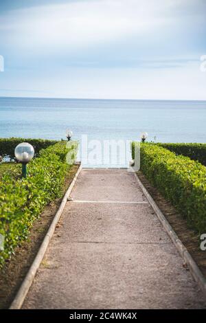 Kleiner Felsenweg mit Büschen links und rechts vor dem Strand im Sommer Stockfoto