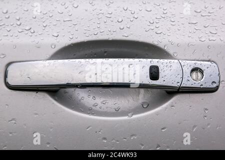 Verchromter Autotürgriff mit Schlüsselloch und Fernbedienung schlüssellose Öffnung Taste Abdeckung der Wassertropfen nach dem Regen, Nahaufnahme. Stockfoto