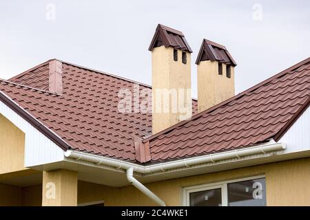 Ein braunes Dach einer Keramikfliese mit einem Rohr ein Sturm Entwässerungssystem, schließen Details der architektonischen Struktur. Stockfoto