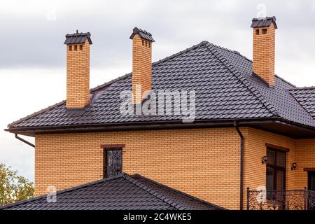 Ein braunes Dach einer Keramikfliese mit einem Rohr ein Sturm Entwässerungssystem, schließen Details der architektonischen Struktur des Ziegelhauses. Stockfoto