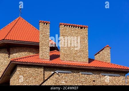 Ein orangefarbenes Dach einer Keramikfliese mit einem Rohr ein Sturmdrainage-System, schließen Details der architektonischen Struktur eines Steinhauses. Stockfoto