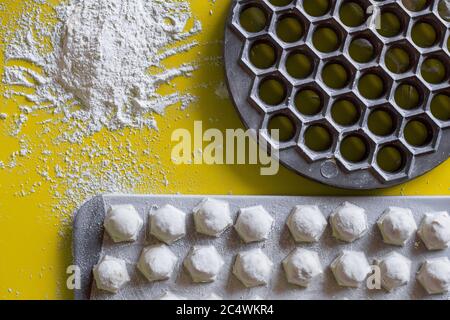 Gestohlene Knödel gefaltet auf einem gelben Tischbrett mit einer Form zum Formen und Mehl, eine Lebensmitteltextur von oben. Stockfoto