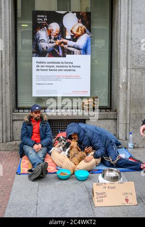 Obdachlose betteln mit ihren Haustieren, unterhalb einer Bankwerbung im Zentrum von Madrid, Spanien. Stockfoto