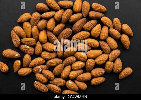 Mandeln auf einem schwarzen Tisch verstreut. Mandel ist ein gesundes vegetarisches Protein nahrhafte Nahrung. Snacks mit Naturnüssen. Stockfoto