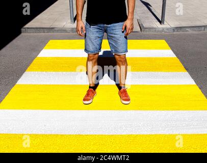 Ein junger Mann in einem schwarzen T-Shirt und Jeans-Shorts Steht an einem Fußgängerübergang Stockfoto