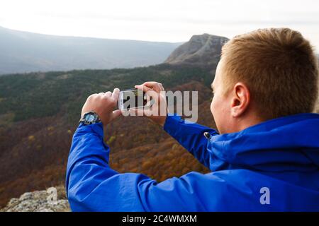 Wanderer sitzen und fotografieren die schöne Berglandschaft mit Handy. Bergsteiger Mann fotografieren Panorama mit Smartphone auf dem Gipfel. Stockfoto