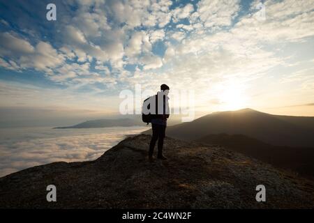 Silhouette des Wanderers mit Rucksack auf der Spitze des Berges stehen und Blick auf schöne gelbe Herbstlandschaft Sonnenuntergang über Wolken Stockfoto