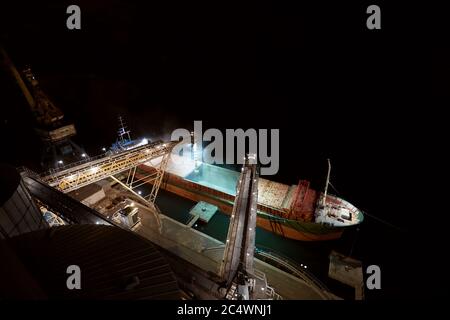 Großer Getreideanleger am Seehafen. Cerealien Massenumladung von der Straße zum Schiff in der Nacht. Beladen von Getreide auf Großfrachter Stockfoto