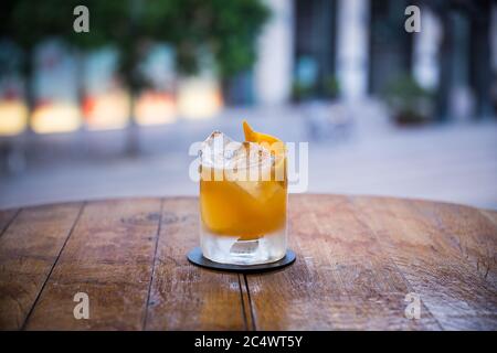 Auf einem Holztisch steht ein leckerer gelber Cocktail auf Eis, der Hintergrund ist verschwommen Stockfoto