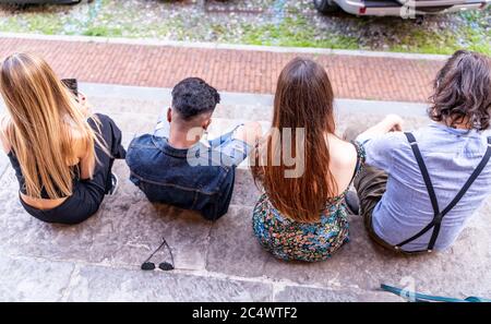 Gruppe von multirassischen Freunden sitzen auf einer Marmortreppe mit Smartphones, um Inhalte in sozialen Netzwerken zu teilen Stockfoto