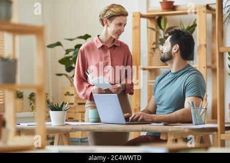 Porträt einer Managerin, die mit einem hübschen bärtigen Mann spricht, der an der Rezeption in einem modernen Bürogebäude mit Holzdetails arbeitet Stockfoto