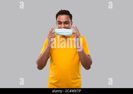 Indischer Mann setzt auf medizinische Maske in Gelb Tshirt isoliert Stockfoto