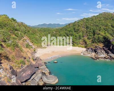 Schöner geheimer Strand Butterfly in Goa, Indien. Luftaufnahme des unberührten Strandes mit felsigen Bucht und Wellen, die zusammenbrechen. Stockfoto