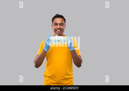 Indian man setzt auf medizinische Maske und Handschuhe in Gelb Tshirt isoliert Stockfoto