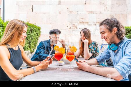 Gruppe von multirassischen Freunden sitzen auf einem Tble im Freien mit Smartphones, um Inhalte in sozialen Netzwerken teilen Stockfoto