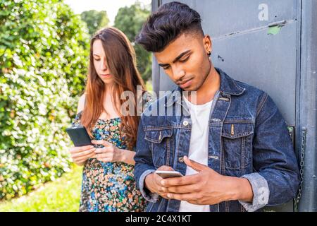 Ein paar multirassische Freunde vor einem Zeitungskiosk, die mit Smartphones Inhalte in sozialen Netzwerken teilen Stockfoto