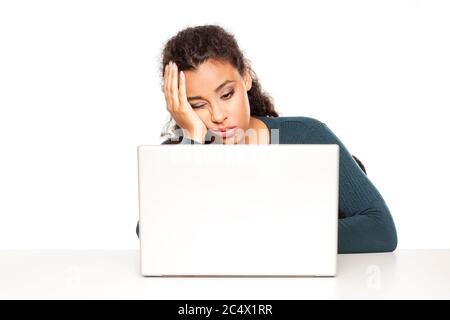 Junge afrikanische müde Frau sitzt an ihrem Schreibtisch vor dem Laptop auf weißem Hintergrund Stockfoto