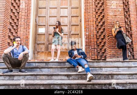 Gruppe von multirassischen Freunden sitzen auf einer Marmortreppe mit Smartphones, um Inhalte in sozialen Netzwerken zu teilen Stockfoto