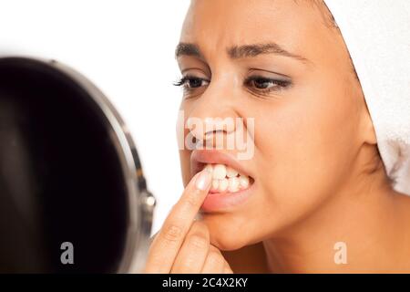 Porträt einer jungen dunkelhäutigen Frau, die mit dem Finger auf weißem Hintergrund ihre Zähne pflückt Stockfoto