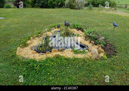 Vorgeformter schwarzer Kunststoff-Gartenteich umgeben von Kiesweg in Rasen, Großbritannien Stockfoto