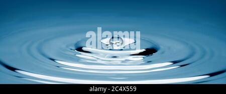 Wassertropfen, der in Wasser fällt und so eine perfekte konzentrische Kreisfläche darstellt. Stockfoto