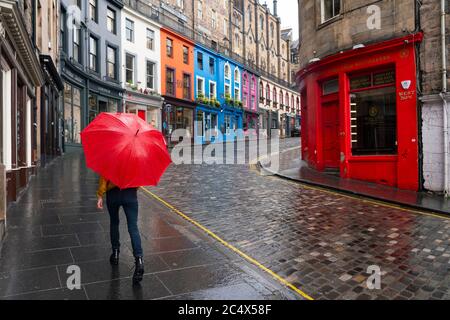 Edinburgh, Schottland, Großbritannien. Juni 2020. 29 Viele Geschäfte, die einen Zugang zur Straße haben, dürfen heute in Schottland für Geschäfte geöffnet werden. Trotz kühler Temperaturen, starker Winde und oft heftigem Regen standen einige Geschäfte morgens Schlange. Die Touristenläden an der Royal Mile blieben jedoch wegen des Mangels an Touristen geschlossen und die Straßen in der Altstadt blieben leer. Im Bild: Ein Mitglied der öffentlichen Spaziergänge in Regen auf der Victoria Street mit den meisten Touristenläden noch geschlossen. Iain Masterton/Alamy Live News Stockfoto