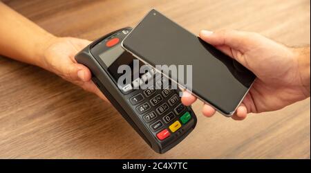 Mobile Bezahlung, Smartphone nfc, drahtlose Nahfeldkommunikation. Kassierer und Kunde reicht mit POS-Maschine und Smartphone, Nahaufnahme vie Stockfoto