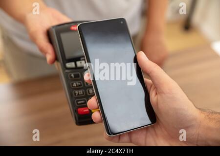 Mobile Bezahlung, Smartphone nfc, drahtlose Nahfeldkommunikation. Kassierer und Kunde reicht mit POS-Maschine und Smartphone, Nahaufnahme vie Stockfoto