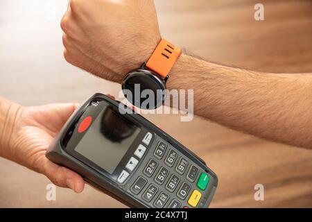 Mobile Bezahlung, Smart Watch nfc, drahtlose Nahfeldkommunikation. Kassierer und Kunden Hände mit POS-Maschine und Smart Watch, closeup vi Stockfoto