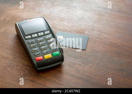 POS-Terminal und Kreditkarte auf Holzhintergrund, Kopierraum.Terminal-Kassenautomat für kontaktloses Bezahlen. Bankausstattung, NFC. Stockfoto