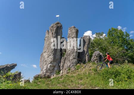 Hübsche ältere Frau unterwegs mit ihrem Elektro-Mountainbike auf einem felsigen Waldweg in der Fränkischen Schweiz, Bayern, Deutschland Stockfoto