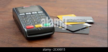 POS-Terminal und Kreditkarten auf Holzhintergrund, Banner. Terminal Kassenautomat für kontaktloses Bezahlen. Bankausstattung, Konsumdenken, sh Stockfoto